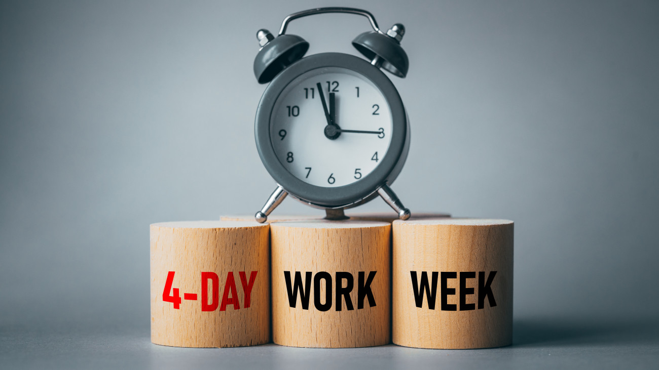 Symbol of a 4-day working week. Desk with wooden blocks with the words 4-day work week, alarm clock and beautiful gray background. Copy space. Business concept, change from 5 to 4 day work week