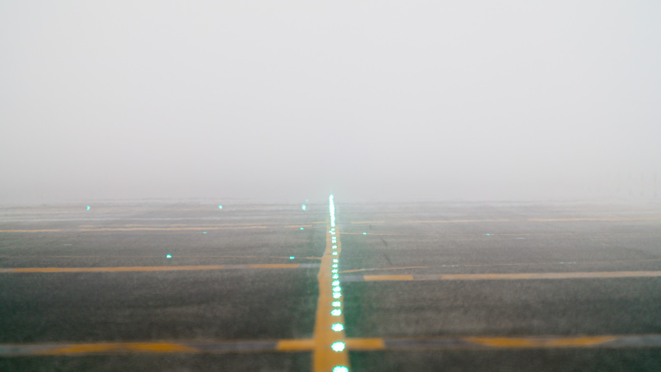 Airport runway lights shining through thick fog, gradually disappearing into the mist, creating an atmospheric and enigmatic scene.