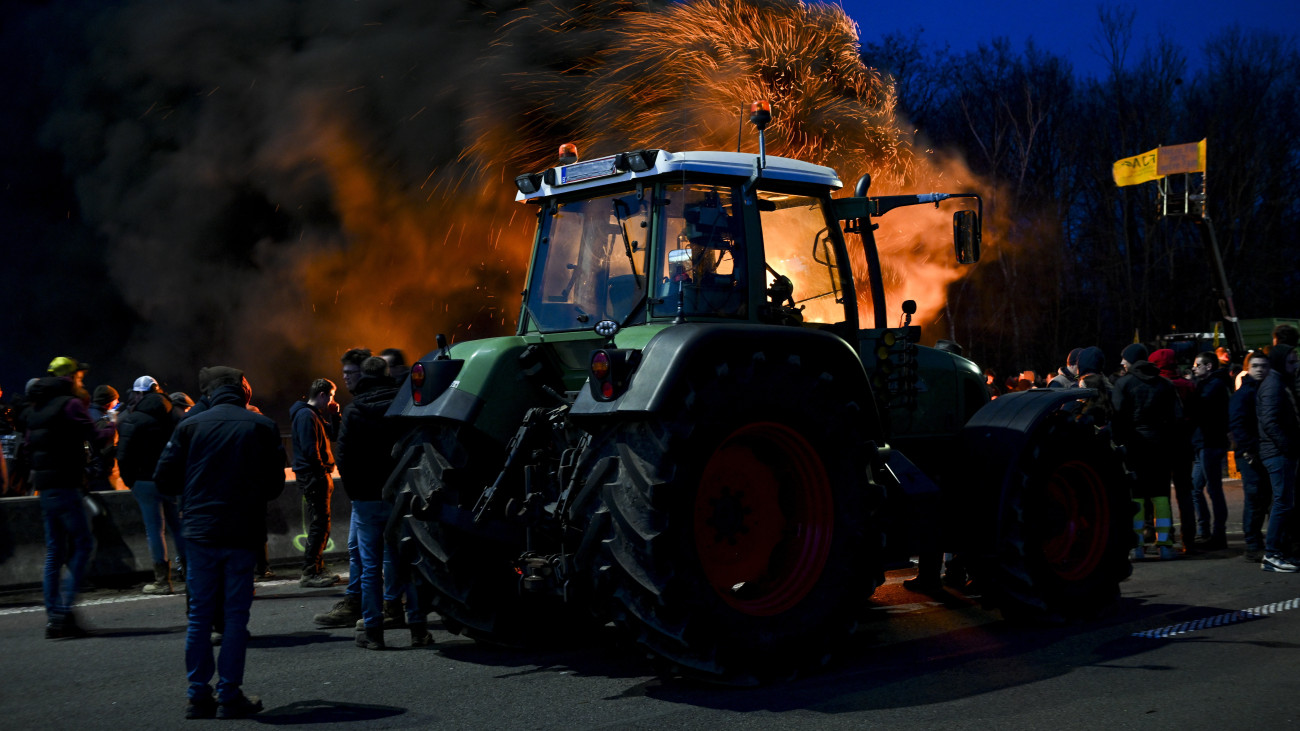 Belga gazdák autógumikat égetnek, miközben traktorjaikkal akadályozzák a forgalmat a Daussoulx közelében lévő autópályán 2024. január 28-án. A belga gazdálkodók a csökkenő bevételeik, a bonyolult jogszabályok és a túl sok adminisztrációs munka miatt tiltakoznak.