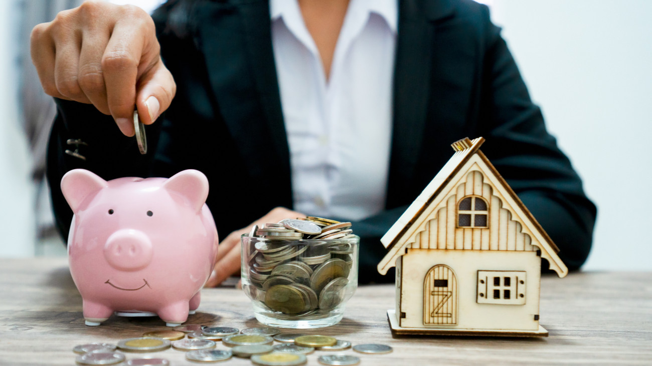 Businessman putting money coins into a pink piggy bank thinking of buying a new house - saving money for future concept and loan for plan business investment for real estate in the future concept.