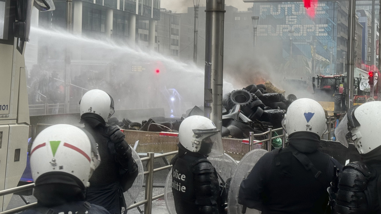 Rendőrök vízágyúval oltják a tüntető gazdák által felgyújtott gumikat a brüsszeli európai negyedben az Európai Unió Mezőgazdasági Tanácsának ülése előtt 2024. február 26-án.