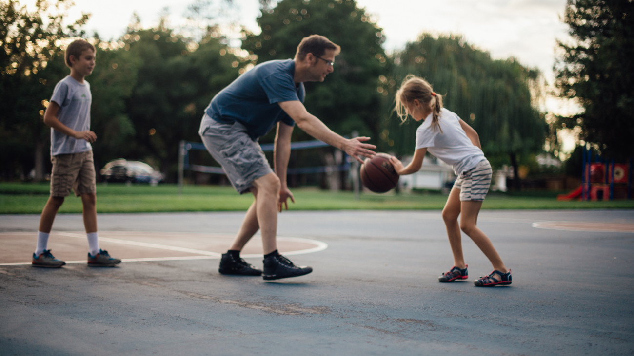 Father and two children playing basketball in a park