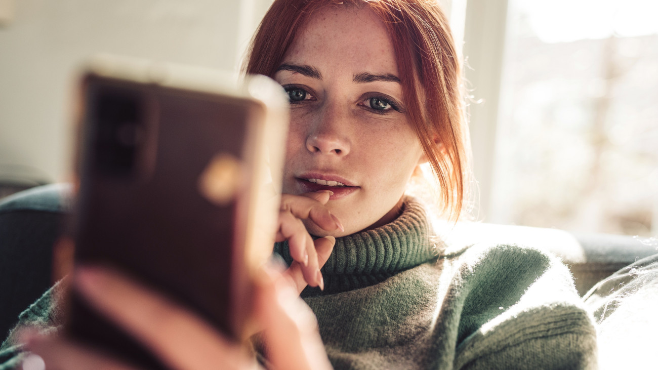 Woman with red hair looking on screen of her mobile phone.