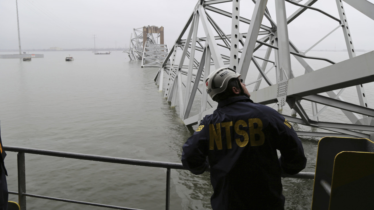 Az amerikai Országos Közlekedésbiztonsági Hivatal (NTSB) képén a hivatal szakértője vizsgálódik a baltimore-i Francis Scott Key híd acélszerkezetének roncsai alá szorult Dali konténerszállító hajón 2024. március 27-én. Március 25-én éjjel a teherhajó egy acél tartóoszlopnak ütközött, és a híd összeomlott. Az ott dolgozó nyolc karbantartó munkás közül kettőt kimentettek, hatan életüket vesztették, négynek a holttestét még keresik.