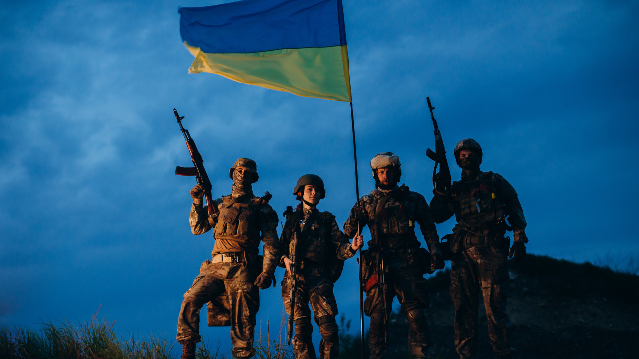 Portrait of four armed Ukrainian militarymen with a national flag in the evening looking at camera