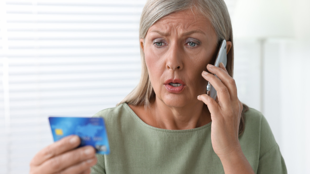 Worried woman with credit card talking on smartphone indoors. Be careful - fraud