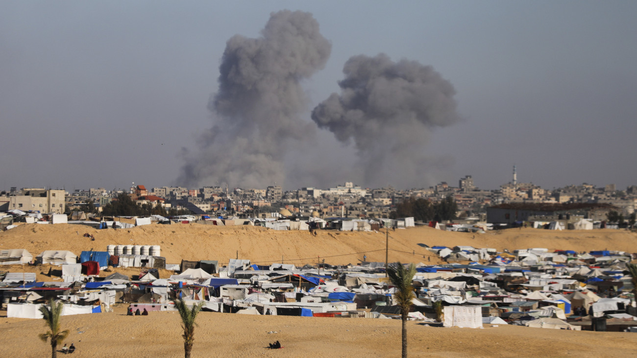 Izraeli légicsapás füstje gomolyog a Gázai övezet déli csücskében levő Rafah város felett, az előtérben palesztin belső menekültek szükségtábora 2024. május 6-án, amikor az izraeli erők műveletet kezdtek az Egyiptommal határos városban. Az izraeli hadsereg felszólította a Rafah keleti lakónegyedeiben levő palesztinokat, hogy meneküljenek a tengerparti al-Mavaszi negyedbe vagy Hán-Júnisz környékére.