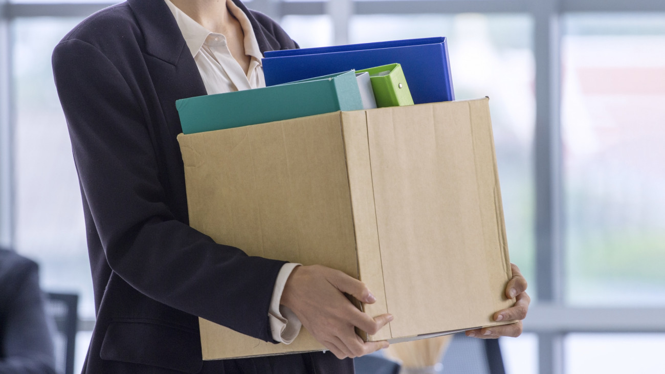 business concept:   An unemployed with her cardboard box walking out of the work office.