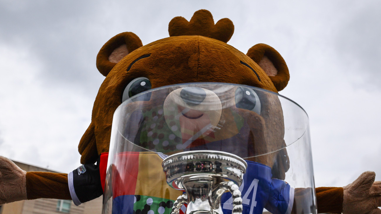 Albärt, a 2024-es németországi labdarúgó-Európa-bajnokság hivatalos kabalafigurája az Henri Delaunay-kupával, a bajnokság trófeájával a berlini Brandenburgi kapu előtt 2024. április 25-én. A kupa végigjárta a 2024-es németországi torna helyszíneit. A tornát 2024. június 14. és július 14. között rendezik Németországban.