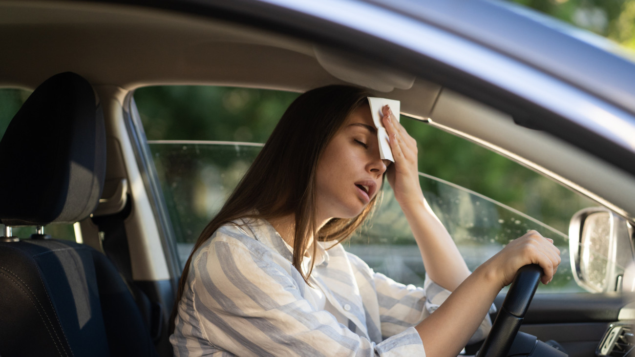 Girl driver being hot during heat wave in car, suffering from hot weather, has problem with a non-working air conditioner, wipes sweat from her forehead with tissue. Summer, heat concept.