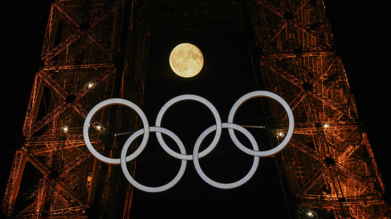 A Hold világít az olimpiai jelképpel díszített párizsi Eiffel-torony mögött 2024. július 22-én, négy nappal a párizsi nyári olimpia kezdete előtt.