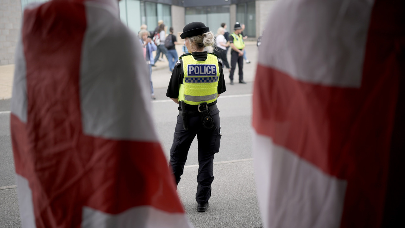 ROTHERHAM, ENGLAND - AUGUST 4: Anti-immigration protesters wearing St. Georges cross flags and police officers stand outside of the Holiday Inn Express in Manvers, which has been used as an asylum hotel, on August 4, 2024 in Rotherham, United Kingdom. Yesterday saw widespread violence as Far-right agitators in Liverpool and Manchester rioted and looted shops. Police were attacked and injured and dozens of arrests were made. (Photo by Christopher Furlong/Getty Images)