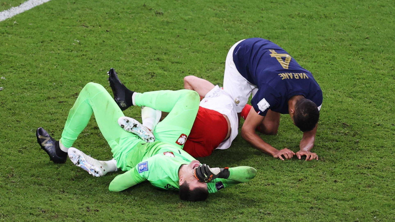 A francia Raphael Varane (j), a lengyel Matty Cash (k) és Wojciech Szczesny kapus (b) a földön a katari labdarúgó-világbajnokság nyolcaddöntőjében játszott Franciaország-Lengyelország mérkőzésen a dohai at-Tumama Stadionban 2022. december 4-én.