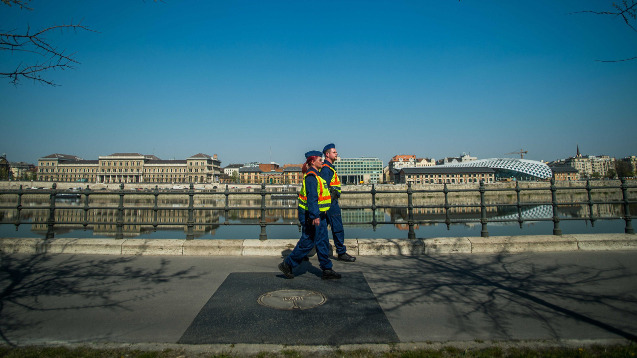 Rendőrök járőröznek a budapesti Műegyetem rakparton 2020. április 8-án. A koronavírus-járvány miatt kijárási korlátozást vezettek be Magyarország egész területére március 28. és április 11. között. Ebben a két hétben az otthonokat, a lakóhelyeket csak munkavégzés vagy az alapvető szükségletek ellátása céljából lehet elhagyni. Az élelmiszerboltokat, drogériákat, patikákat 9 és 12 óra között kizárólag a 65 év felettiek látogathatják. A rendőrség a közterületeken megnyugtató, segítő, empatikus és lojális intézkedésekkel sarkallja a lakosságot a kijárási korlátozás betartására.
