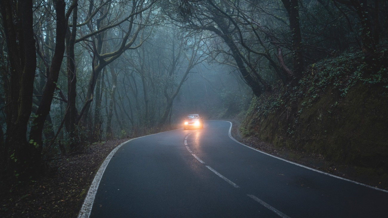 Autó alkonyatkor egy ködös hegyi úton.